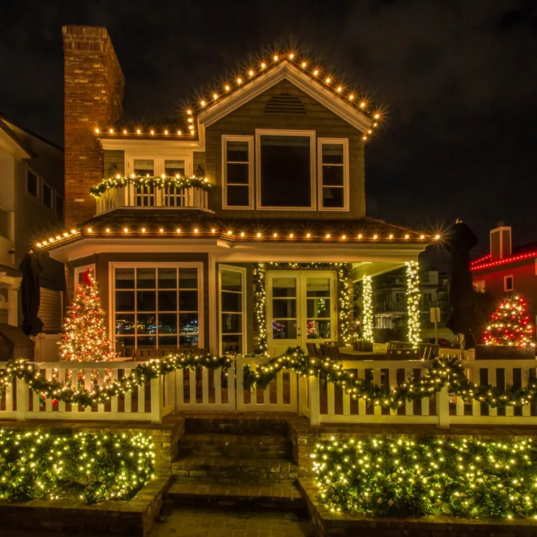 A cozy home decorated with holiday lights and a lit picket fence